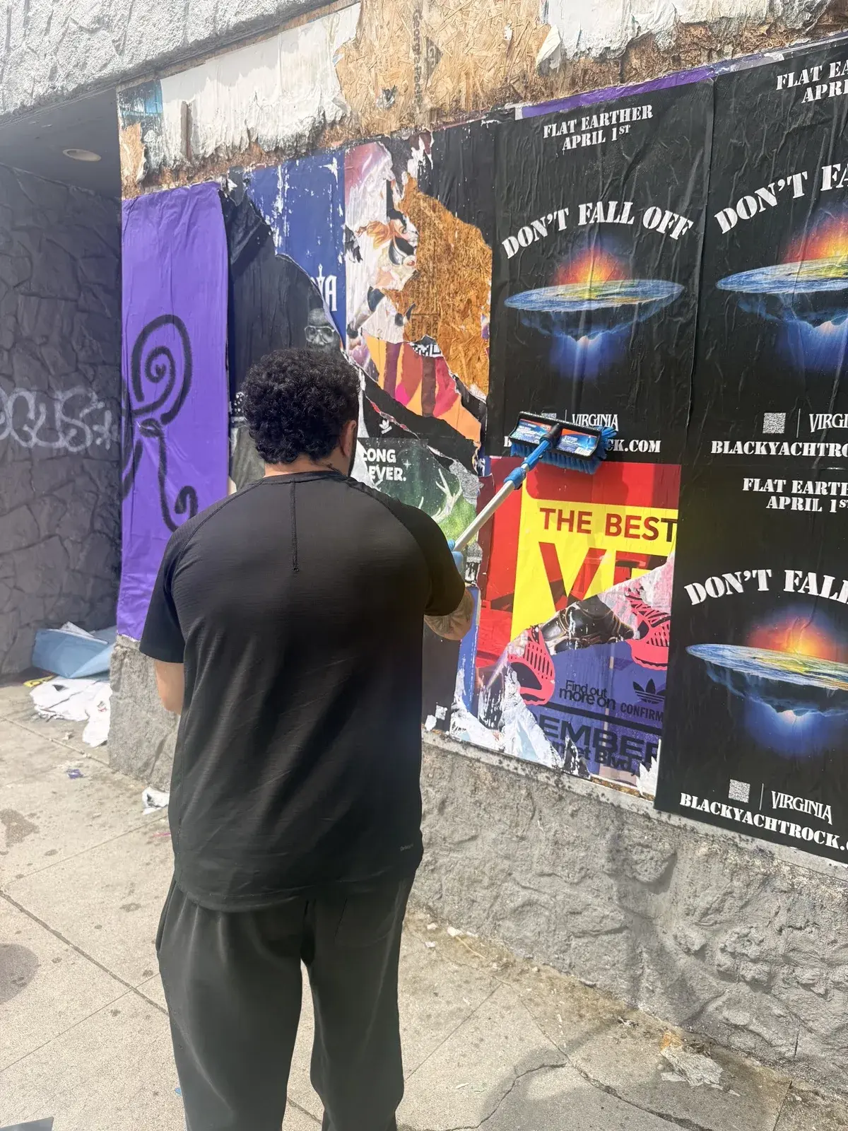 Pedestrian walking past Don't Fall Off wheat paste poster wall street art installation